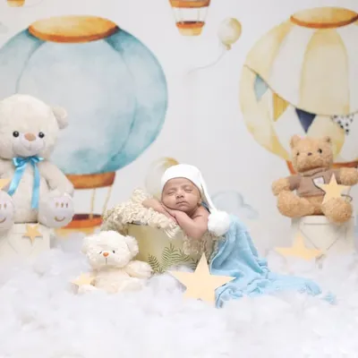 A dreamy hot air balloon adventure. This whimsical setup features a baby sleeping in a basket amongst the clouds, surrounded by teddy bears and stars.