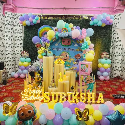 A complete Cocomelon themed first birthday party setup. This package includes a large, vibrant backdrop with characters, an organic balloon garland in pastel colors, Cocomelon foil balloons, and marquee letters spelling out the birthday child's name.