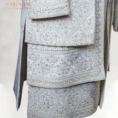 This image showcases the layering and detail of a custom wedding sherwani. Notice the intricate, all-over embroidery that flows seamlessly from the body to the sleeves and the matching stole (dupatta), creating a cohesive and majestic groom's outfit.