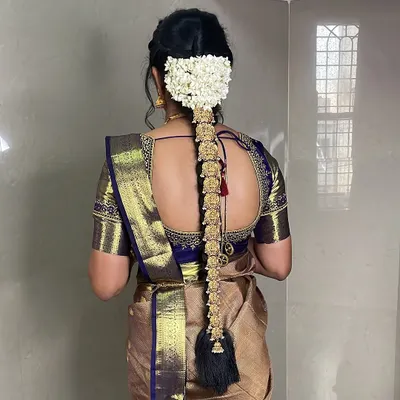 A classic South Indian bridal hairstyle. This long braid is adorned with traditional gold jada billai and fresh jasmine flowers, creating a truly regal look.