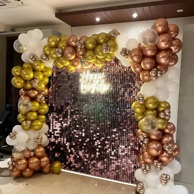 This is a full view of the rose gold sequin wall with a balloon garland. The combination of chrome gold, rose gold, and white balloons creates a rich, celebratory feel. The 'Happy Birthday' neon sign adds a warm, inviting light, perfect for evening parties.