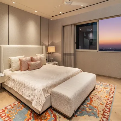 This guest bedroom in a Gurugram residence is designed for comfort and style. The soft pastel furnishings and artwork are complemented by a rich, dark veneer wall panel that adds contrast and depth, creating a warm and inviting atmosphere.
