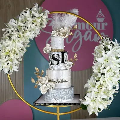 A masterpiece for a love that shines. This silver and pearl-themed wedding cake, framed by a floral hoop, combines intricate textures, delicate sugar flowers, and shimmering details for a look of timeless elegance.