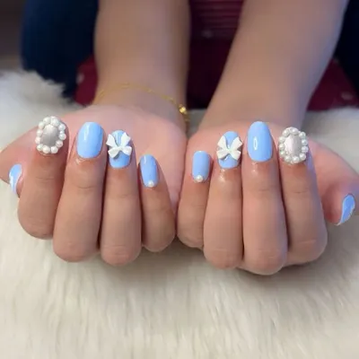 A classic coquette nail set. This design features a soft baby blue polish with hand-sculpted 3D white bows and elegant pearl-framed accent nails for a touch of vintage charm.