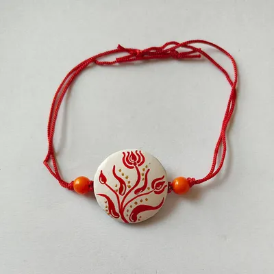 This handmade terracotta rakhi features a delicate red floral design on a white background, inspired by Bengali alpona. It's an elegant and artistic choice for this special festival.