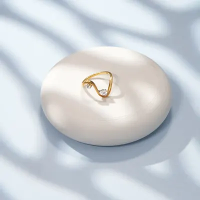A minimalist shot of a delicate gold ring on a white pedestal, with soft, leaf-like shadows. This elegant and serene composition is perfect for fine jewellery brands.