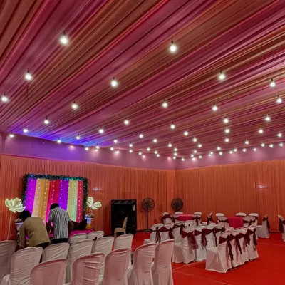 An indoor Mehendi setup with a colorful striped backdrop. We arranged seating for guests with simple white covers and maroon bows, keeping the focus on the vibrant stage.