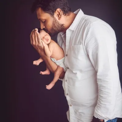 A father's gentle kiss for his newborn. This powerful image captures the profound bond between a dad and his baby in a simple, classic portrait.