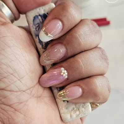A beautiful example of a modern, elegant manicure. This set features a mix of French tips with a gold chrome line, a sheer pink with a single floral gem, and a subtle gold flake accent.