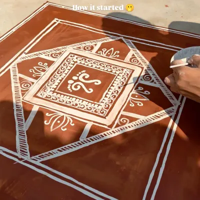 This image shows the process of creating a Mandana, a traditional floor painting from Rajasthan. Here, I am drawing the central motif of Goddess Lakshmi's footprints, a symbol of prosperity, using a cloth dipped in white paste.