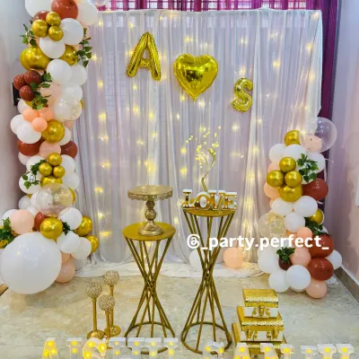 This is a perfect example of a personalized anniversary setup for your home. It includes a beautiful balloon garland, a fairy light curtain backdrop, and the couple's names in large light-up letters, creating a custom photo corner.