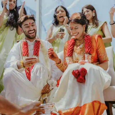 A candid and joyful moment from a South Indian wedding, where the couple and their friends are laughing during a ceremony.