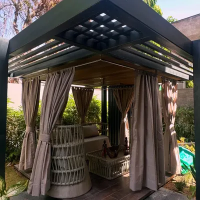 A full view of the custom pergola I designed in Jaipur. It features a slatted roof for partial shade and can be enclosed with curtains, creating a versatile outdoor room surrounded by lush greenery.
