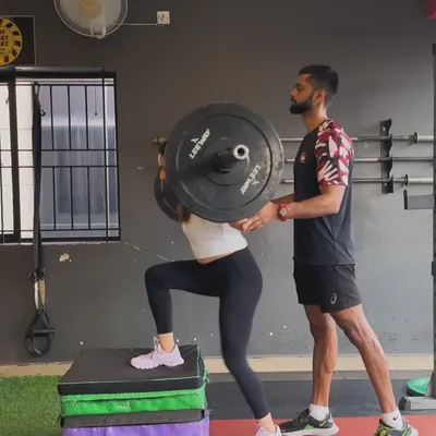 Perfecting the weighted step-up. A coach stands by to ensure flawless form and safety as this client builds single-leg strength and stability, a crucial component of a balanced lower-body program.