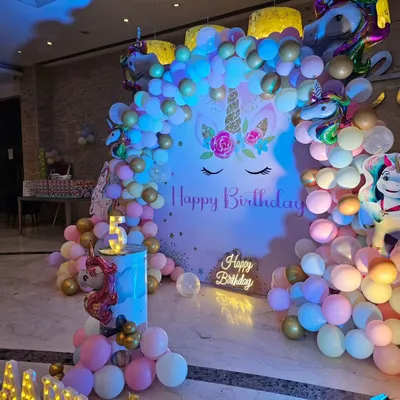 A magical Unicorn-themed 5th birthday party, featuring a large backdrop, a pastel and gold balloon garland, and a light-up 'Happy Birthday' sign.