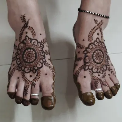 A classic and elegant foot mehndi design. The central mandala is surrounded by delicate leafy vines, and the toes are fully covered for a traditional finish.