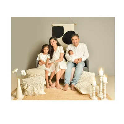 A serene family portrait with a modern, bohemian aesthetic, featuring parents and their two children in coordinating white outfits against a backdrop of neutral tones and textures.
