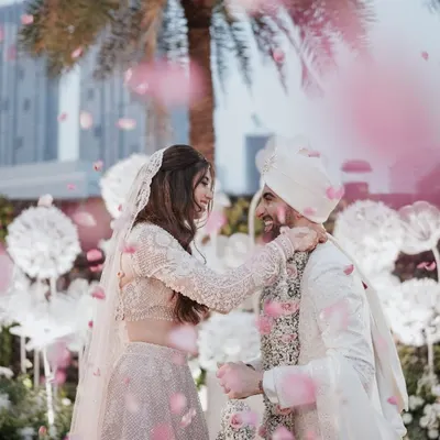 A moment of pure cinematic romance. Rose petals shower the couple as they share a joyful, loving glance during their varmala ceremony, creating a perfect, fairy-tale image.