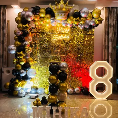 A glamorous 8th birthday with a gold shimmer wall. This stunning setup includes a black, gold, and silver balloon arch, a crown foil balloon, a neon sign, and large light-up letters for the name 'MIHIKA'.