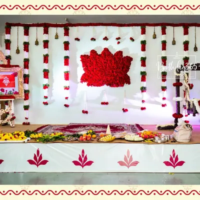 A classic and sacred backdrop for a Namakaran ceremony. The design features a large lotus created from red rose petals, with hanging garlands of red and white flowers and traditional brass bells.