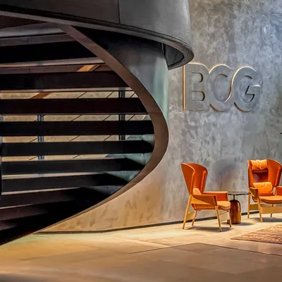 The lobby of the BCG Headquarters in Mumbai features a dramatic spiral staircase set against textured concrete walls, immediately establishing a departure from the typical corporate aesthetic.