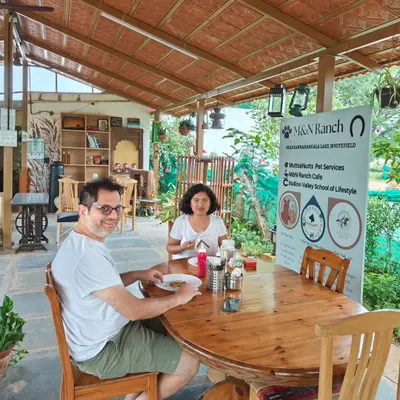 A couple enjoys a peaceful meal at a wooden table in our rustic, covered cafe area. Our space is designed to help you unwind and reconnect with nature, away from the hustle of city life.