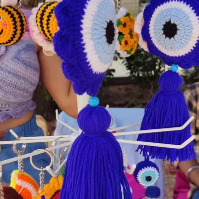 My crochet evil eye wall charm hanging at my market stall. This larger "Nazar" charm comes with a tassel and is perfect for hanging on a wall, in a car, or on a door to protect your space.