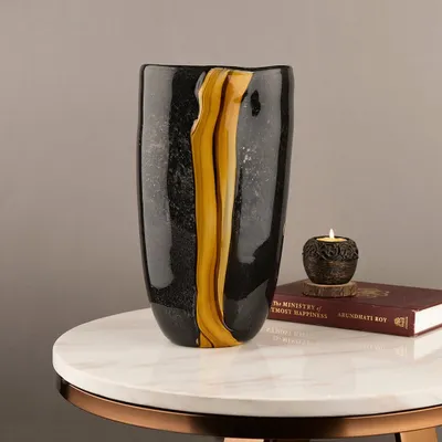 This handblown glass vase features a dramatic streak of gold running through a black, textured body. It's a subtle yet stunning piece that looks beautiful on its own or with a simple flower stem.