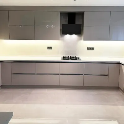 A perfect example of minimalist design in this Gurgaon kitchen, featuring handle-less cabinetry in a glossy beige finish. The continuous under-cabinet LED lighting illuminates the white quartz countertop, creating a clean and spacious feel.