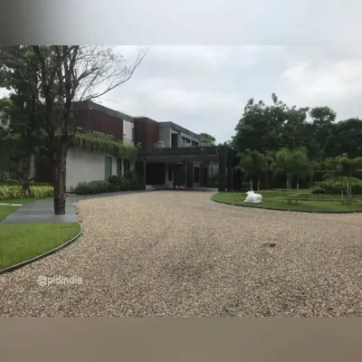 The expansive gravel driveway provides a clean, modern approach to this home in Ahmedabad. The driveway is bordered by a lush lawn and carefully placed trees, creating a natural and understated sense of arrival.