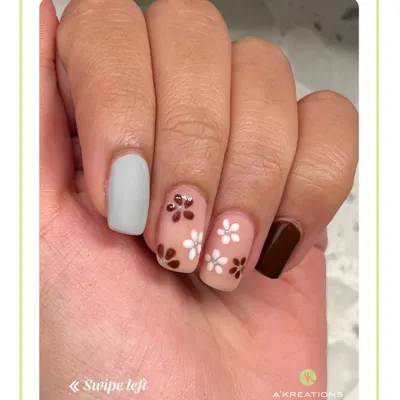 An earthy and chic manicure featuring delicate hand-painted white and brown flowers on a sheer base, complemented by solid grey and brown accent nails.