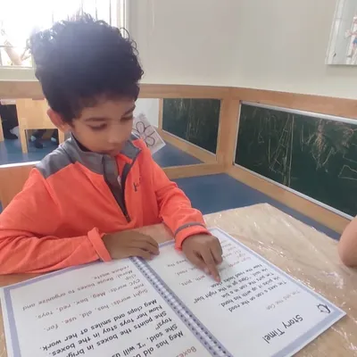 A young boy points to the words as he reads, a key step in developing tracking skills and one-to-one correspondence in our literacy program.