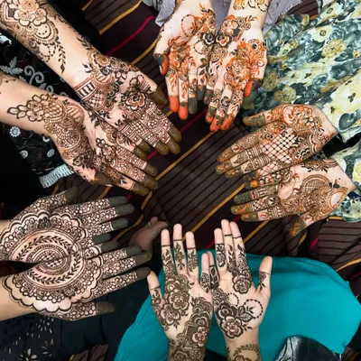 A beautiful shot of a group henna session in progress. Each person has a unique design, from intricate florals to bold mandalas, showing the variety I can offer for your party.