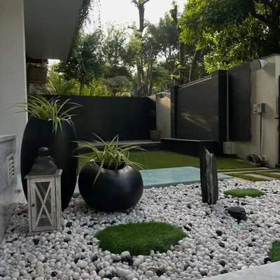 A tranquil Zen garden at the entrance of a Noida home. This design uses a bed of white pebbles, moss patches, and sculptural black planters to create a sense of calm and mindfulness from the moment you arrive.