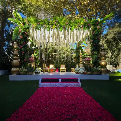 This grand wedding mandap, set against our lush greenery with a dramatic rose petal aisle, showcases how we create breathtaking focal points for your ceremony.