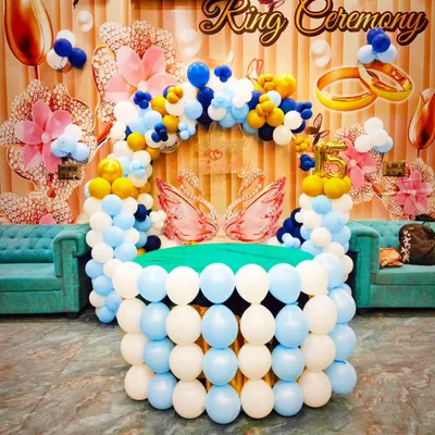 A beautiful and elaborate setup for a ring ceremony. This decoration features a table made of balloons and a colorful balloon arch in blue, white, and yellow, with swan and ring details.