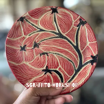 This is a perfect example of a finished Sgraffito plate. The intricate floral pattern was carefully carved by a student, and after firing and glazing, the design really comes to life with a rich, vibrant finish.