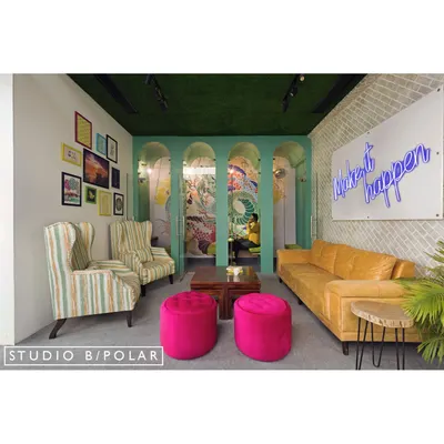 This lounge area in a coworking space we designed uses a mix of colorful furniture, a neon sign, and varied seating to create a welcoming and dynamic environment. The arched glass partitions provide a sense of openness while defining the zone.