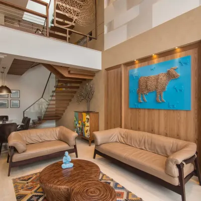 The double-height living area of Kavyam Residence blends warmth and creativity. A bright blue artwork featuring a cow stands out as the main feature, reflecting the client's personal taste and adding a unique, artistic touch to the room.