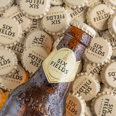 A top-down shot for Six Fields beer, using a bed of bottle caps to create texture and brand reinforcement. The water droplets on the bottle add a refreshing, chilled look that is instantly appealing.