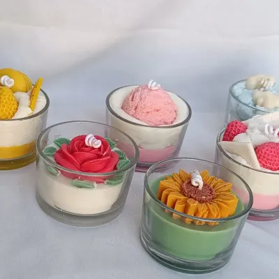 I offer a wide variety of dessert-themed candles. This image shows a collection including a mango dessert candle, a strawberry ice cream scoop, a cloud candle, a rose cake candle, and a sunflower candle.