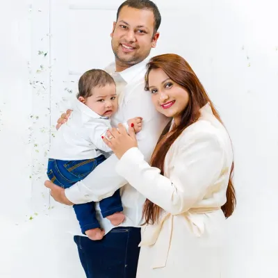 A beautiful, classic family portrait with parents and their baby, all dressed in coordinated white outfits against a clean, bright backdrop. This is a timeless style for any family album.
