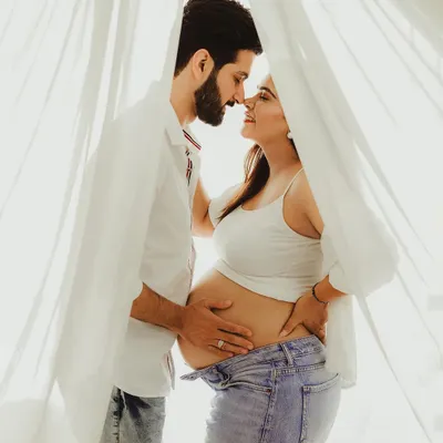 A beautiful, intimate moment from a lifestyle maternity session. The soft, natural light from the window and the casual outfits create a relaxed and authentic feel.