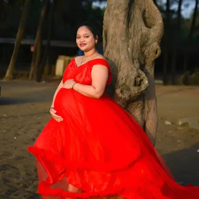 A beautiful outdoor maternity portrait taken at the beach. The vibrant red gown stands out against the natural backdrop, highlighting the baby bump and the mother's radiant smile.