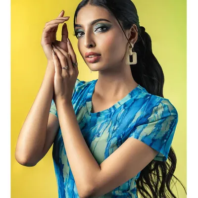 A vibrant studio portrait featuring a model in a blue and green patterned dress against a bright yellow backdrop. Her confident pose and the bold color contrast create a fresh and modern fashion statement.
