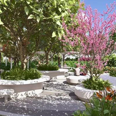 This seating plaza in the Kriya Villa development features curved, built-in benches nestled under flowering trees, creating an intimate and beautiful space for community interaction.