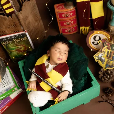 Ready for the Hogwarts Express! This little wizard is sleeping soundly with his magic wand, surrounded by props that bring the world of Harry Potter to life in this themed baby photoshoot.