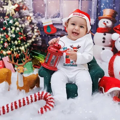 The happiest baby celebrating his first Christmas, holding a lantern in a festive winter wonderland setup.