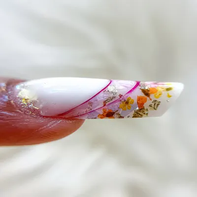 A close-up of an intricate inbuilt nail art design. This technique involves encapsulating dried flowers and foil flakes within the nail extension for a beautiful, dimensional effect.