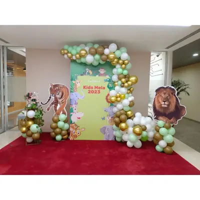 This jungle themed entrance was created for a "Kids Mela 2023" event. It includes a custom printed backdrop, large animal cutouts of a lion and tiger, and a balloon garland in green, gold, and white.